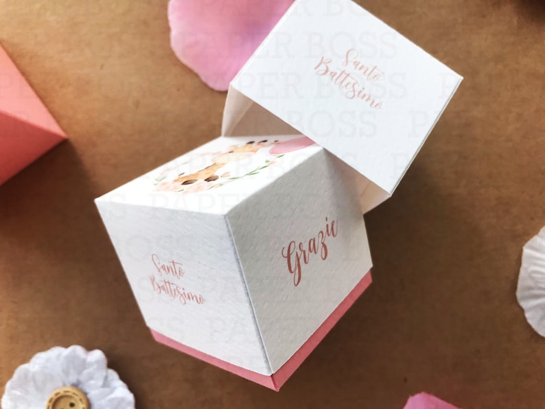 Peut inclure: Bo&icirc;te &agrave; drag&eacute;es blanche avec un ruban rose et le texte "Santo Battesimo" et "Grazie" en cursive. La bo&icirc;te est d&eacute;cor&eacute;e d'un motif floral avec une illustration aquarelle d'un cerf.