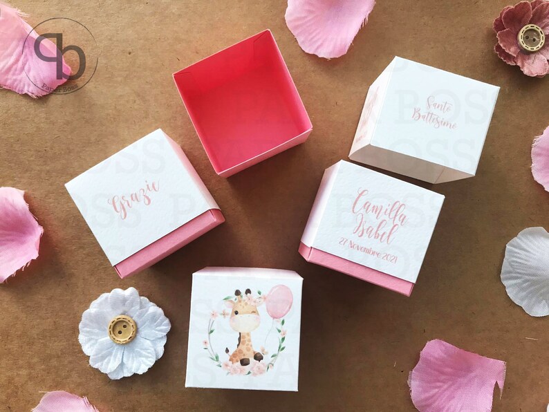 Peut inclure: Bo&icirc;tes de drag&eacute;es roses et blanches avec un motif de girafe. Les bo&icirc;tes portent les inscriptions "Grazie", "Camilla Isabel", "21 Novembre 2021" et "Santo Battesimo".