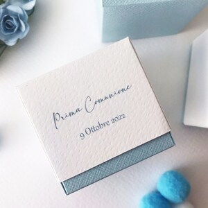 May include: A white gift box with a blue lid. The box is decorated with the text "Prima Comunione" and the date "9 Ottobre 2022".