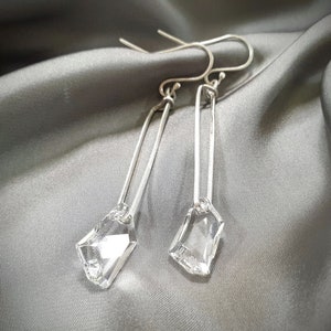 May include: A pair of silver earrings with clear crystal drops. The earrings are long and dangle, with a simple, minimalist design.