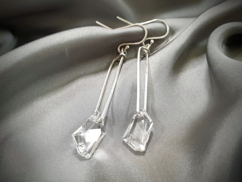 May include: A pair of silver earrings with clear crystal drops. The earrings are long and dangle, with a simple, minimalist design.