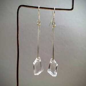 May include: A pair of silver dangle earrings with clear crystal geometric pendants. The earrings are hanging from a silver stand.