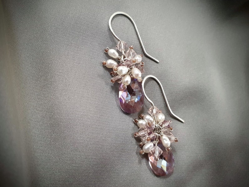 May include: A pair of silver dangle earrings with a cluster of pink and white beads and a teardrop-shaped crystal.