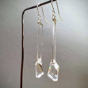 May include: A pair of silver earrings with clear crystal drops hanging from a silver bar.