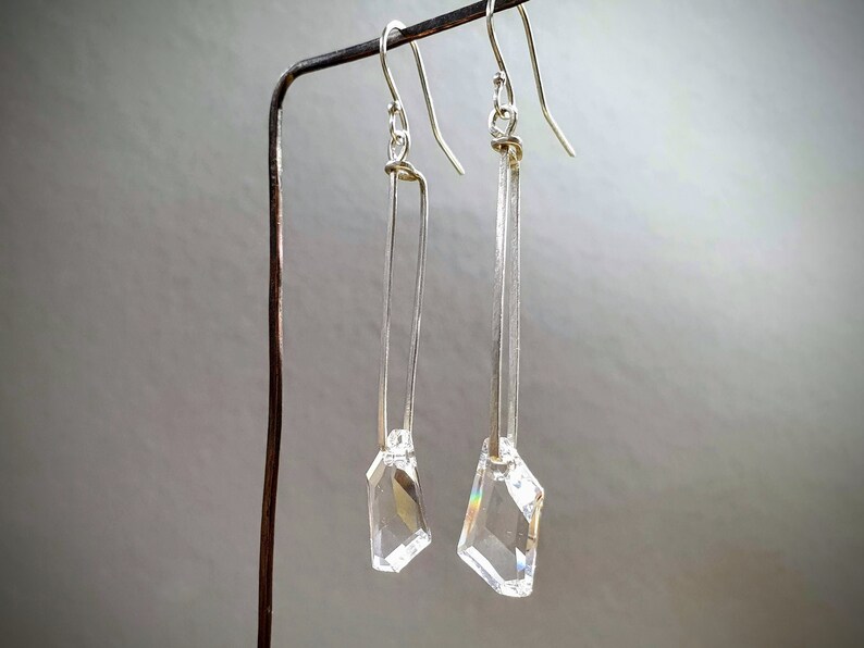 May include: A pair of silver earrings with clear crystal drops hanging from a silver bar.