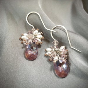 May include: A pair of silver dangle earrings with a cluster of purple, white, and clear crystals hanging from each earring.
