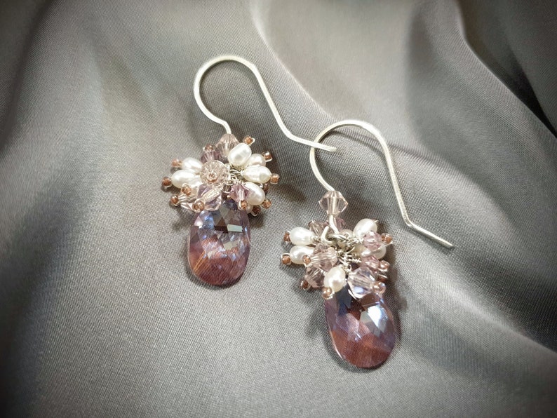 May include: A pair of silver dangle earrings with a cluster of purple, white, and clear crystals hanging from each earring.