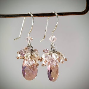 May include: A pair of dangle earrings with pink and white beads and a teardrop-shaped crystal.