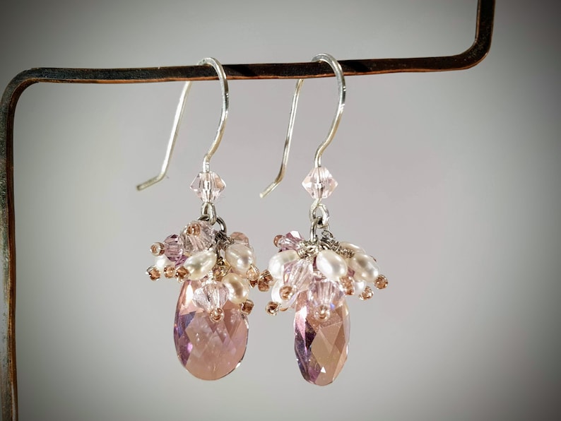 May include: A pair of dangle earrings with pink and white beads and a teardrop-shaped crystal.