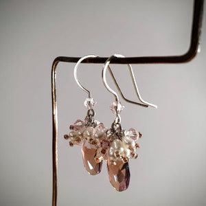 May include: A pair of dangle earrings with pink and white beads and a teardrop-shaped crystal.