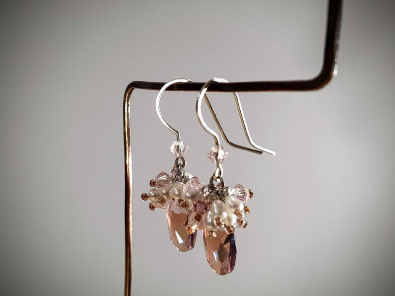 May include: A pair of dangle earrings with pink and white beads and a teardrop-shaped crystal.