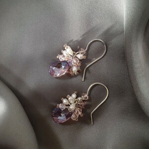 May include: A pair of dangle earrings with a cluster of small pink and white beads and a larger purple crystal drop.