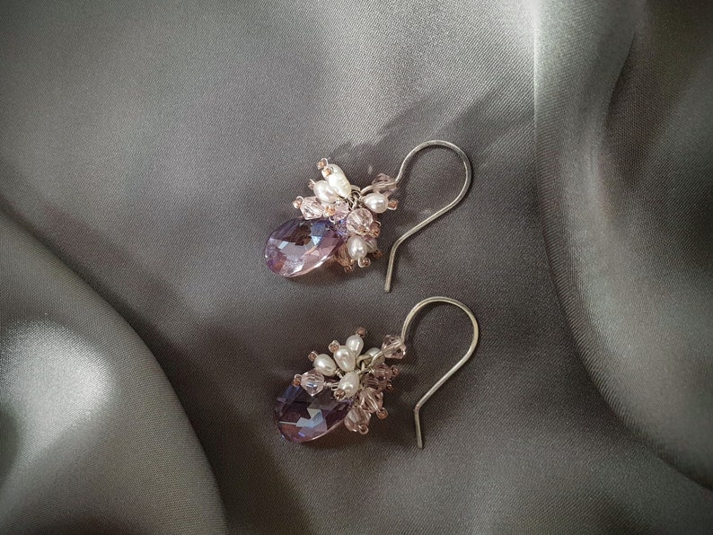 May include: A pair of dangle earrings with a cluster of small pink and white beads and a larger purple crystal drop.