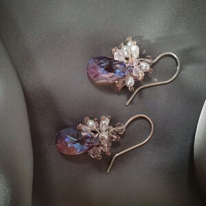 May include: A pair of dangle earrings with a teardrop-shaped purple and blue crystal accented with white pearls and pink beads.