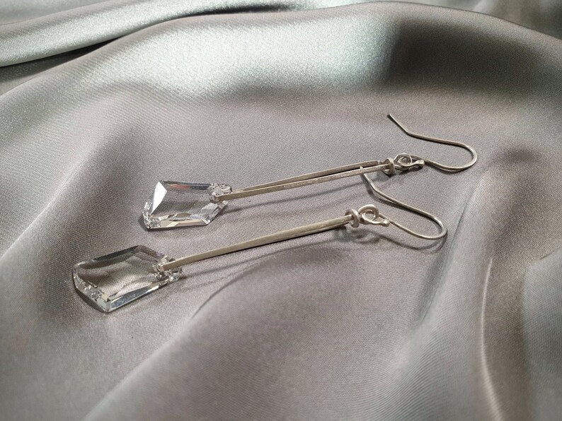 May include: A pair of silver dangle earrings with clear crystal teardrop-shaped stones.