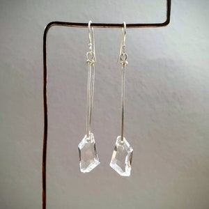 May include: A pair of silver dangle earrings with clear crystal teardrop-shaped charms.