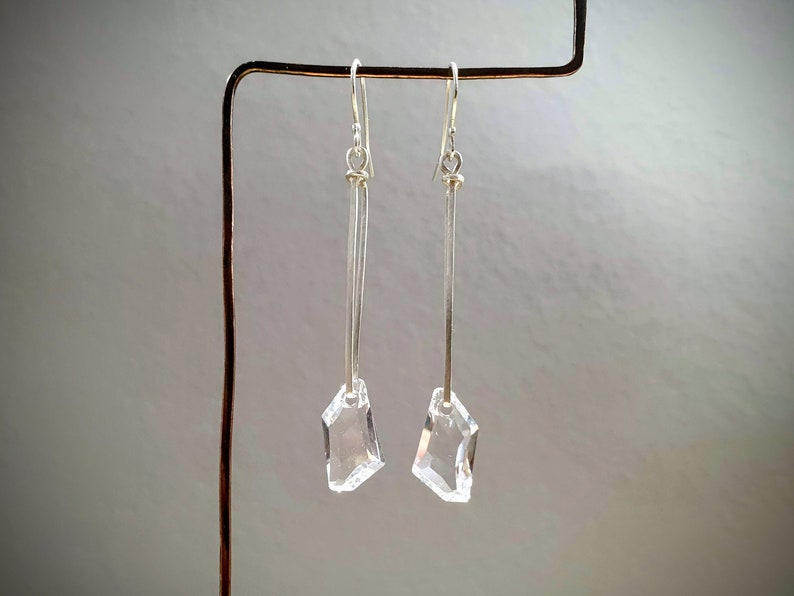 May include: A pair of silver dangle earrings with clear crystal teardrop-shaped charms.