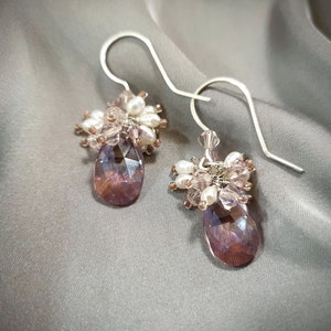 May include: A pair of silver dangle earrings with a teardrop-shaped purple crystal and a cluster of white and pink beads.