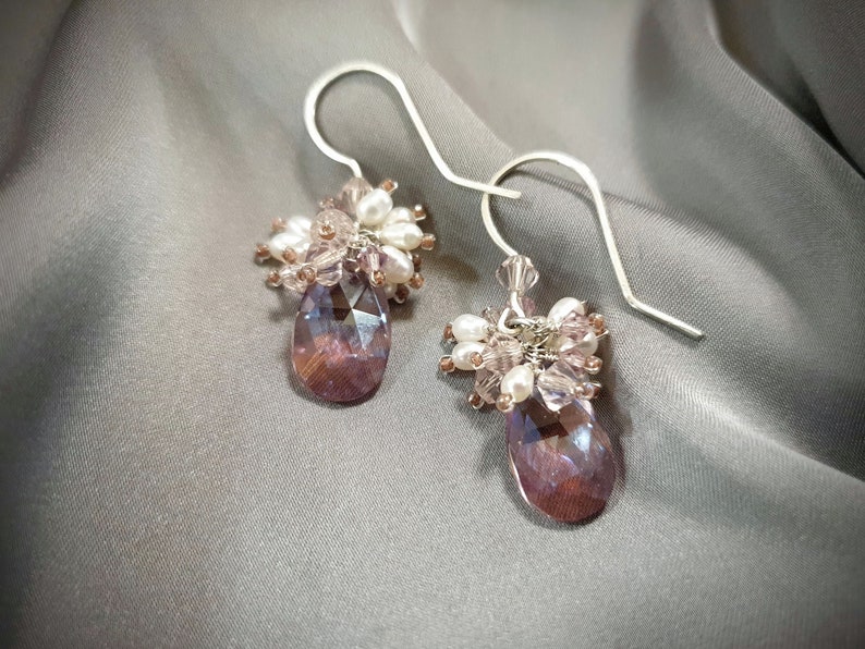 May include: A pair of silver dangle earrings with a teardrop-shaped purple crystal and a cluster of white and pink beads.