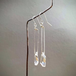 May include: A pair of silver dangle earrings with clear crystal drops. The earrings are hanging from a silver wire.