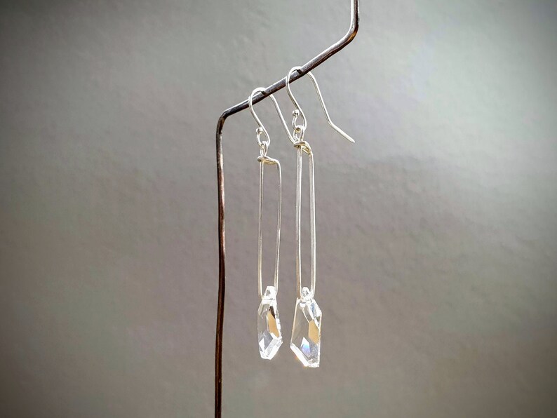 May include: A pair of silver dangle earrings with clear crystal drops. The earrings are hanging from a silver wire.
