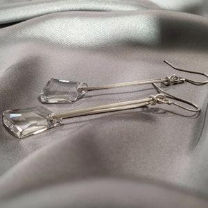 May include: A pair of silver dangle earrings with clear crystal teardrop-shaped stones.