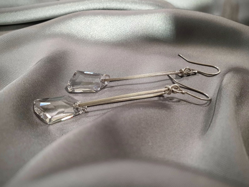 May include: A pair of silver dangle earrings with clear crystal teardrop-shaped stones.