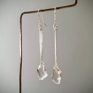 May include: A pair of silver dangle earrings with clear crystal teardrop-shaped stones at the bottom.