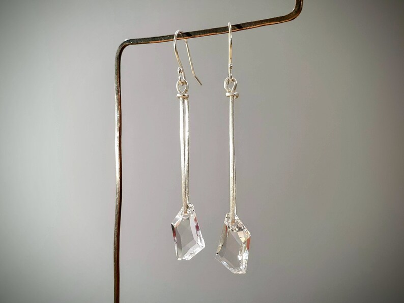 May include: A pair of silver dangle earrings with clear crystal teardrop-shaped stones at the bottom.