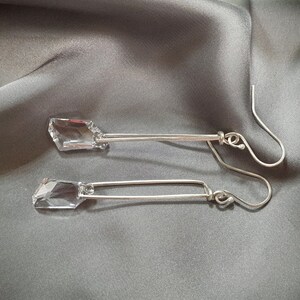 May include: A pair of silver earrings with clear crystal stones hanging from the bottom. The earrings are long and dangle.