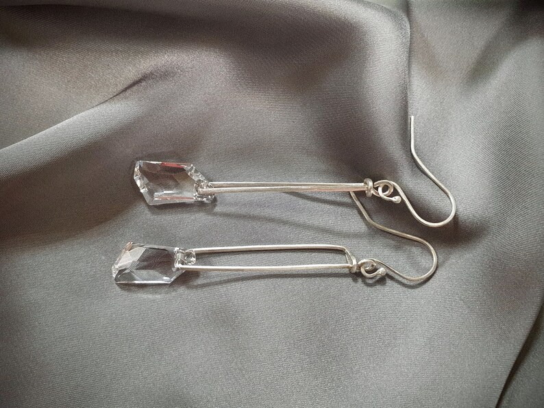May include: A pair of silver earrings with clear crystal stones hanging from the bottom. The earrings are long and dangle.