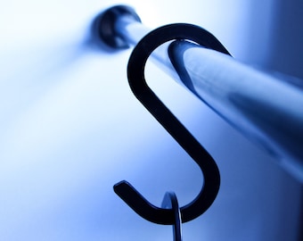 Könnte beinhalten: Nahaufnahme eines schwarzen S-förmigen Hakens aus Metall, der an einer silbernen Metallstange befestigt ist. Der Haken ist zum Aufhängen von Gegenständen an der Stange gedacht.