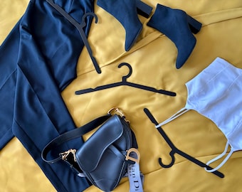 Könnte beinhalten: Eine flache Anordnung von Kleidungsstücken auf einer gelben Oberfläche. Die Artikel umfassen eine schwarze Hose, ein weißes Tanktop, eine schwarze Lederhandtasche mit einer goldenen Kettenkette und drei schwarze Kleiderbügel. Die Handtasche hat ein Etikett mit der Aufschrift "Christian Dior Paris".