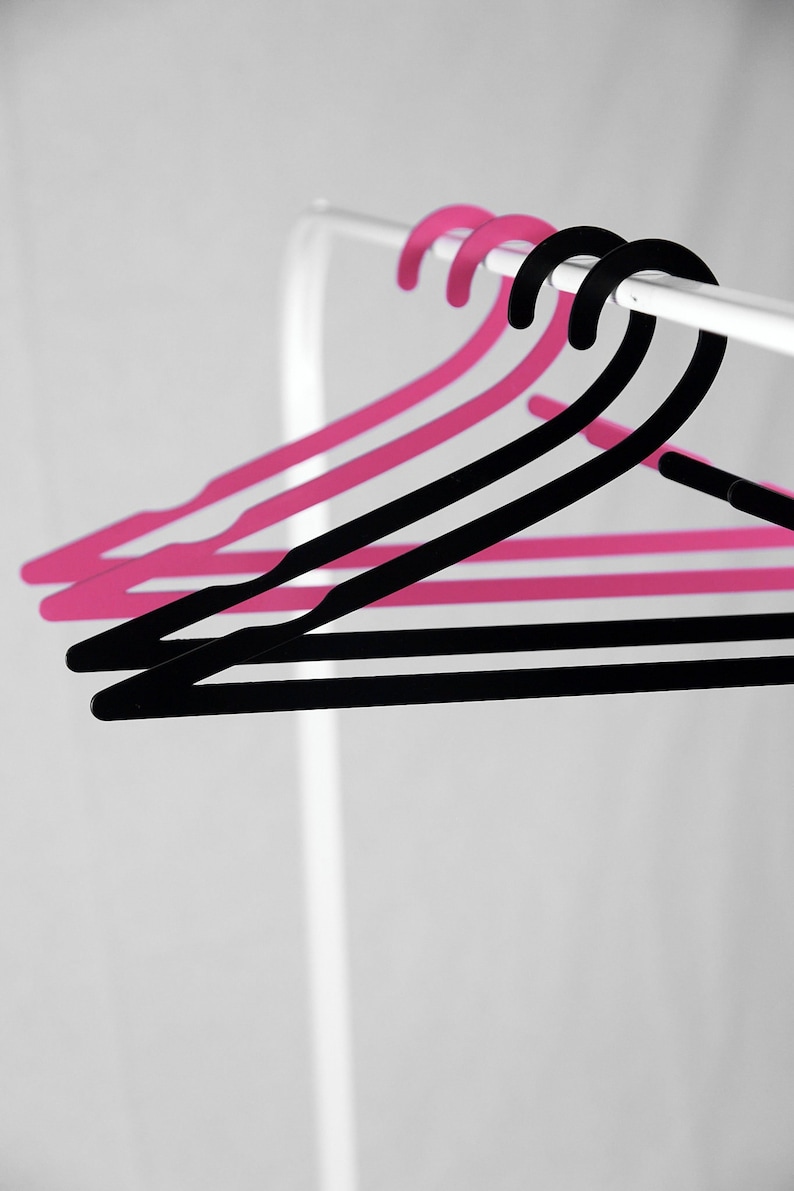 May include: Three hangers, two pink and one black, hang on a white rod.