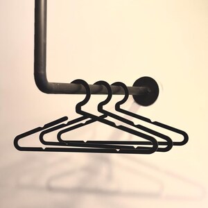 May include: Four black plastic hangers hanging on a black metal rod.