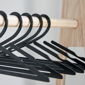May include: A set of black plastic hangers, hanging on a wooden rod. The hangers are arranged in a row, with the hooks facing the same direction.