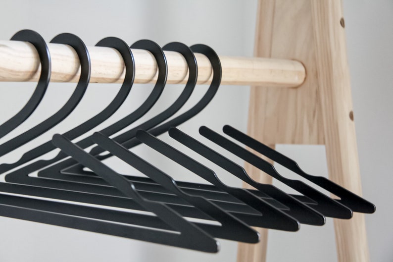 May include: A set of black plastic hangers, hanging on a wooden rod. The hangers are arranged in a row, with the hooks facing the same direction.