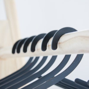 May include: A close-up of a wooden rod with multiple black hangers hanging from it. The hangers are made of a smooth, matte black material and have a simple, modern design.