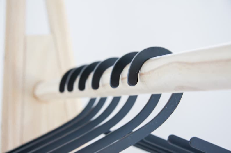 May include: A close-up of a wooden rod with multiple black hangers hanging from it. The hangers are made of a smooth, matte black material and have a simple, modern design.