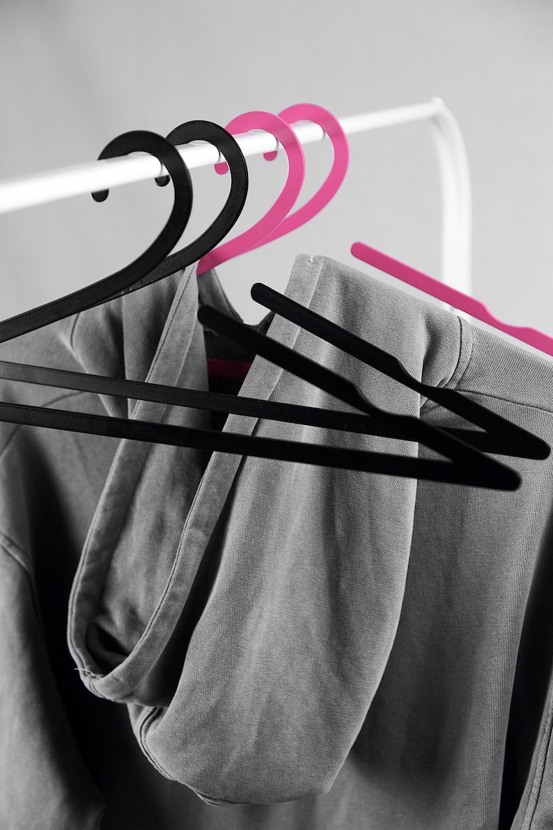 May include: A gray hooded sweatshirt hanging on two black and two pink plastic hangers.