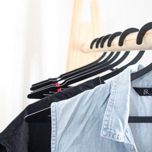 May include: A wooden clothing rack with black hangers holding a blue denim shirt and a black t-shirt. The denim shirt has a black label with the text "B.H.S."