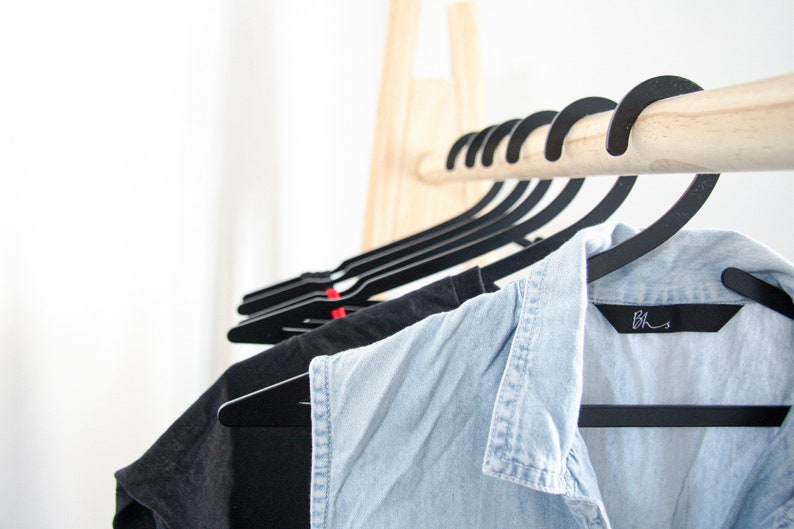 May include: A wooden clothing rack with black hangers holding a blue denim shirt and a black t-shirt. The denim shirt has a black label with the text "B.H.S."