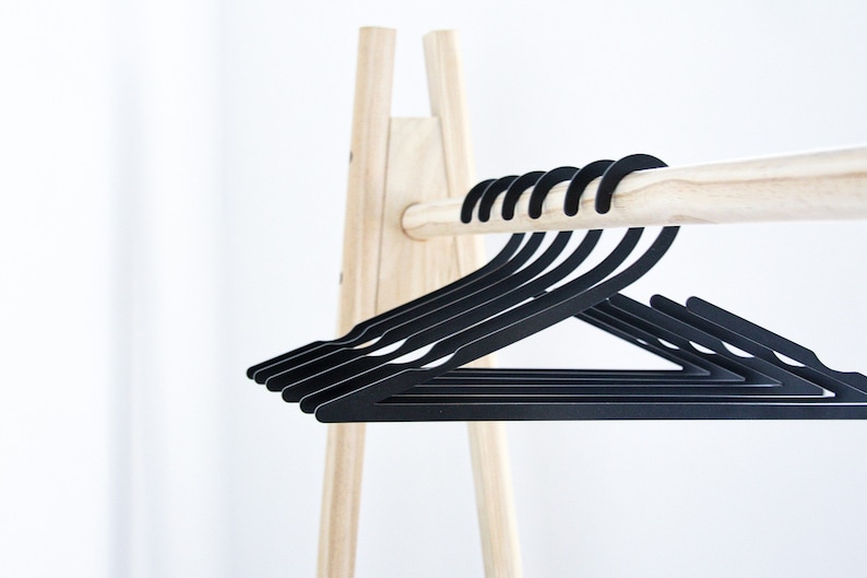 May include: A wooden clothes rack with a set of black plastic hangers. The hangers are stacked on top of each other and are hanging from the rack.