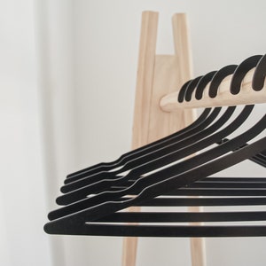 May include: A wooden clothes rack with a row of black plastic hangers. The hangers are arranged in a neat row, with the hooks facing forward.