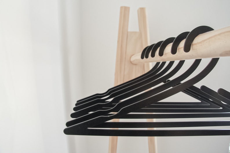 May include: A wooden clothes rack with a row of black plastic hangers. The hangers are arranged in a neat row, with the hooks facing forward.