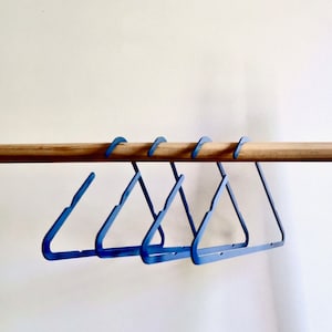 May include: Five blue plastic hangers hanging on a wooden rod.