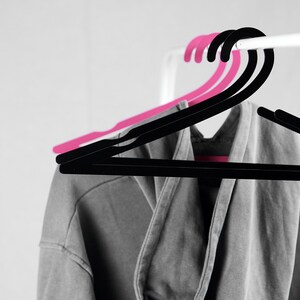 May include: A gray hooded sweatshirt hanging on a black and pink clothes hanger.