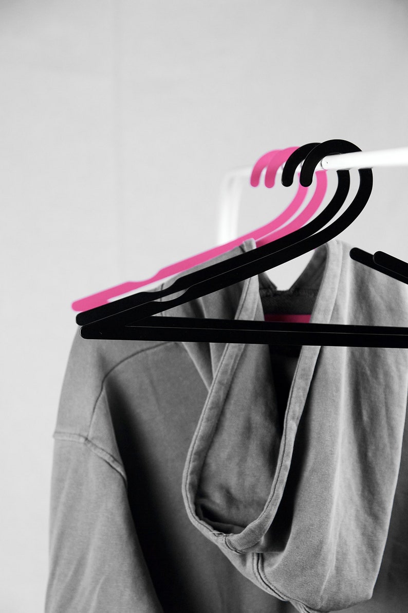 May include: A gray hooded sweatshirt hanging on a black and pink clothes hanger.
