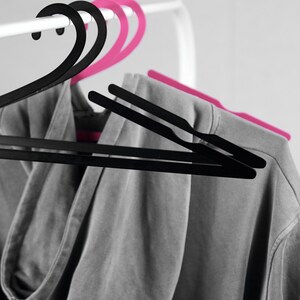 May include: A gray hooded sweatshirt hanging on a white clothes rack with two black and two pink plastic hangers.