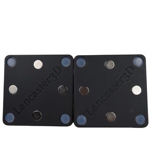 May include: Two black square components featuring the text Lancaster3D, each equipped with four small circular blue pads at the corners and three metallic circular magnets arranged in a triangular pattern on the flat surface.